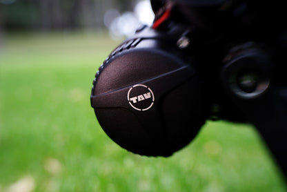 Close-up of the TAV logo on a sleek, black mid-drive motor housing of an e-bike, with a blurred green natural background emphasizing the focus on the detailed craftsmanship.